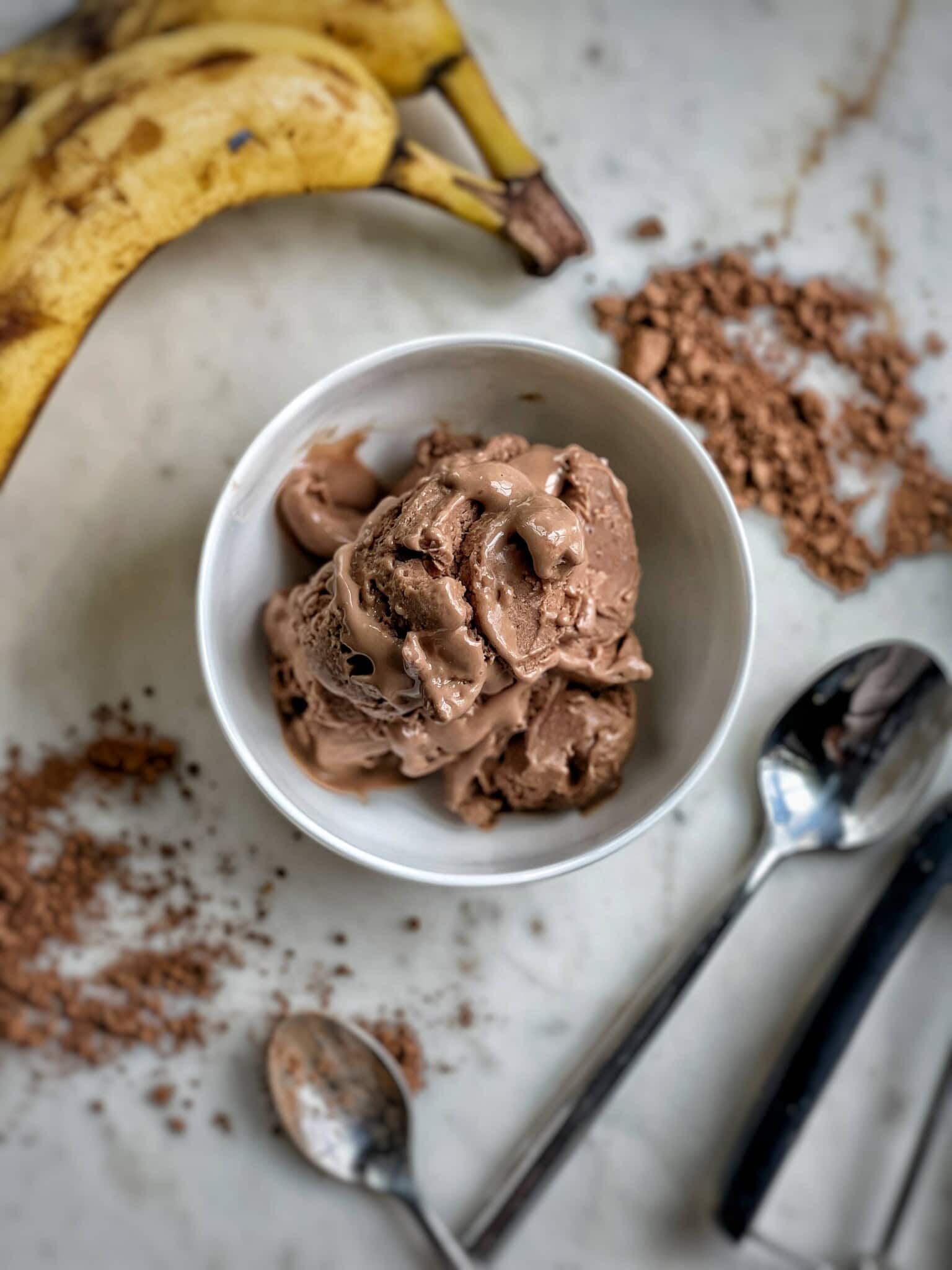 Chocolate peanut butter cottage cheese ice cream in a bowl on a counter top with ingredients spread around.